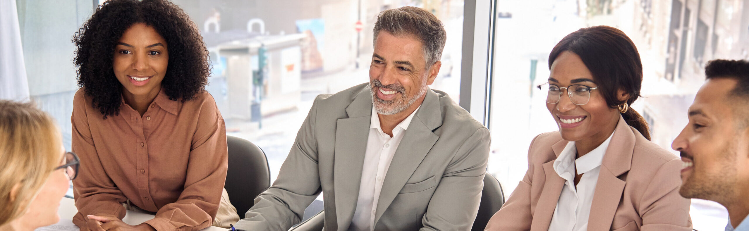Happy diverse executive business people group working together at meeting in boardroom office. International busy board team colleagues company employees collaborating consulting at conference table.