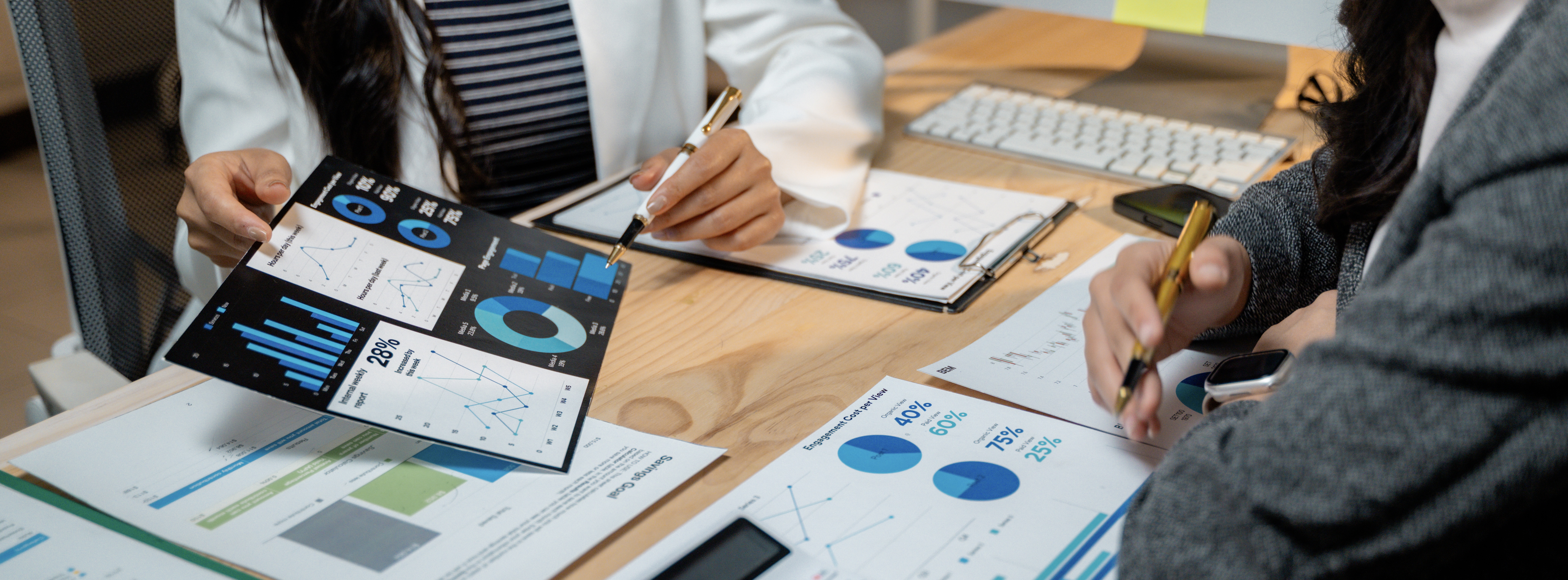 Businesswomen working together analyzing financial charts and graphs using calculator and computer at office desk